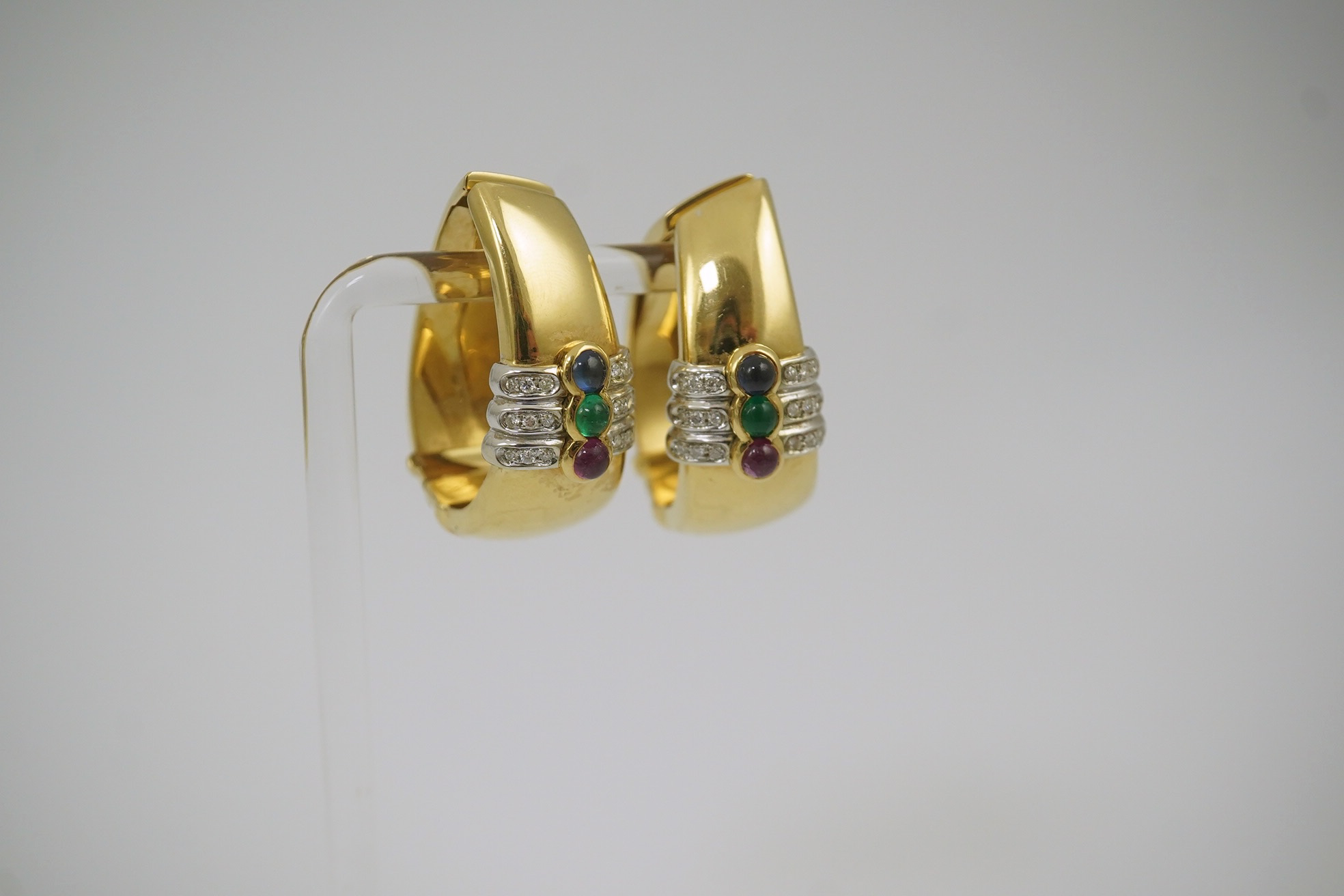 A large modern pair of Mappin & Webb 18ct gold, cabochon ruby, emerald and sapphire and diamond chip set oval loop earrings